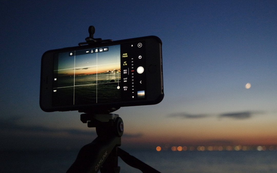 Photo of a smart phone sitting horizontally on a tripod taking a video of a sunset.